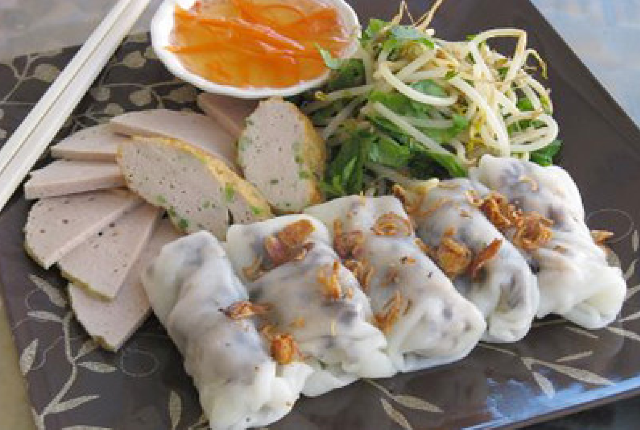 5 pieces of Banh cuon, with side dishes like vegetables and a fish sauce dip placed on a plate 
