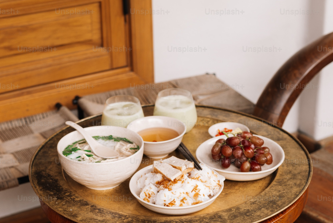 Vietnamese meal on a small table, include a bowl of pho, meat, two drinks and a plate of grapes