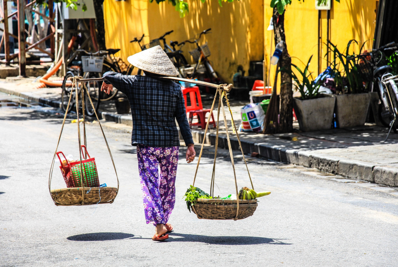 Woman carries a bamboo carrying pole full of their ingridients while walking on the street