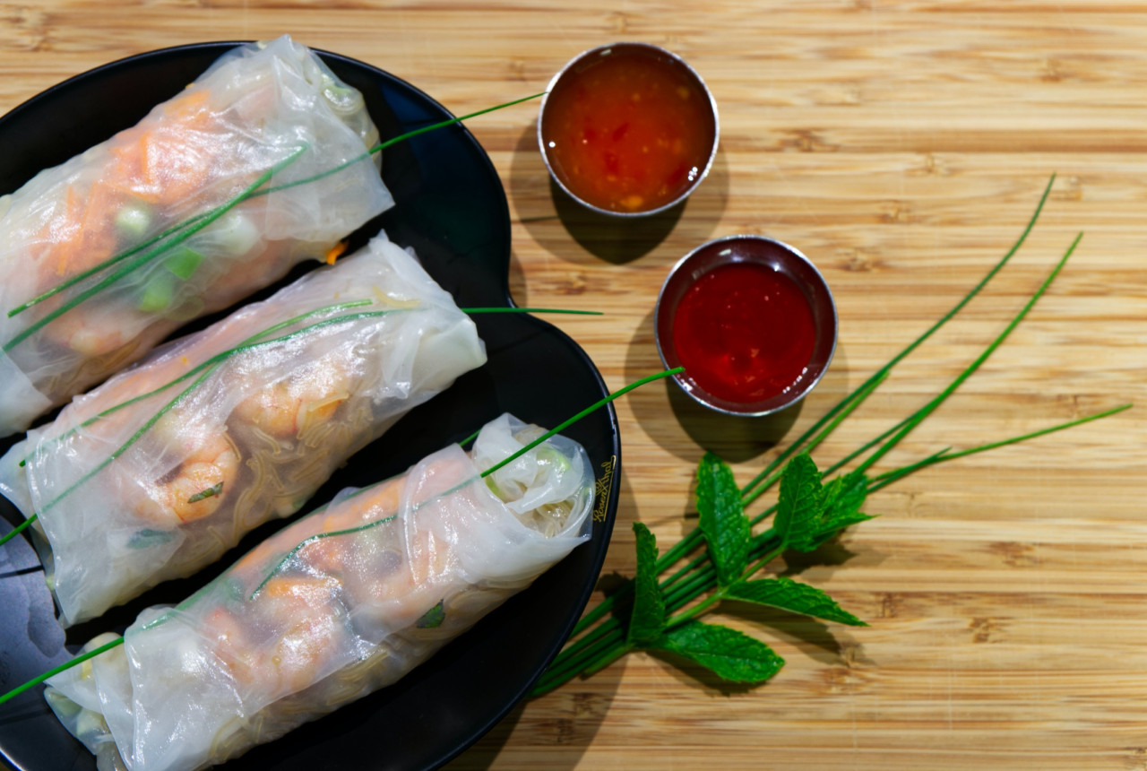 Three servings of fresh spring rolls with side dipping sauces are arranged on a plate